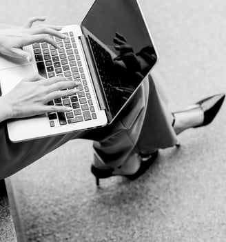 A top-view shot of a woman's well-manicured hands typing on her laptop wearing pointed-toe black heels
