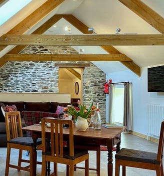 A table and chairs in a room with timber beams and a stone wall