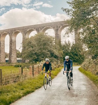 two people riding bikes down a path with a bridge in the background