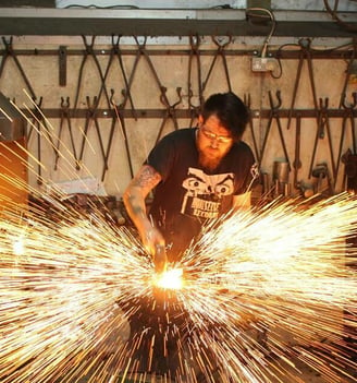 A man is working on a piece of metal at a forge