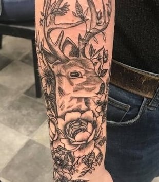 a tattoo of flowers and a buck cover self harm scarring on the arm of a white person