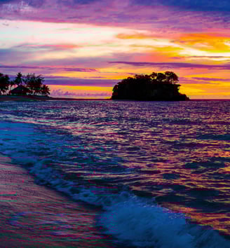 a sunset on a beach with a small island in the background