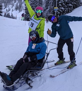 alt="Sean in his sit ski with Outdoors for All instructors Kristin and Ted, posing for the camera