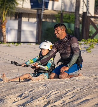 criança sentada na praia aprendendo kitesurf com o instrutor.