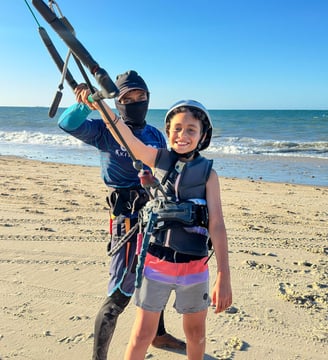 criança em pé na praia aprendendo kitesurf com o instrutor.