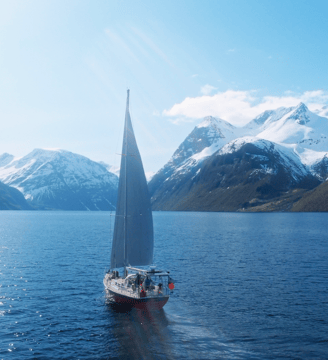 a sailboat sailing on a fjord with mountains in the background | ski and sail in the Lyngen Alps