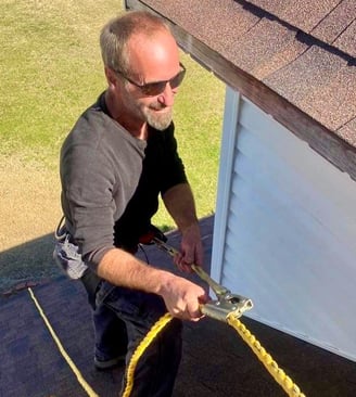 Brett Wilson man holding yellow rope on shingle roof wearing sunglasses