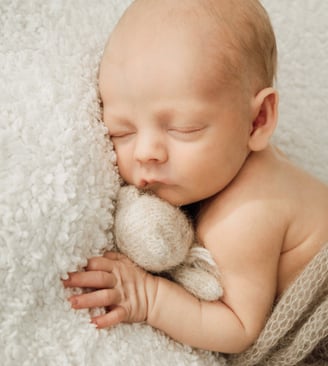 a newborn baby sleeping baby in a blanket and a teddy bear