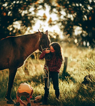 a woman is standing in the grass with a horse, dog and child