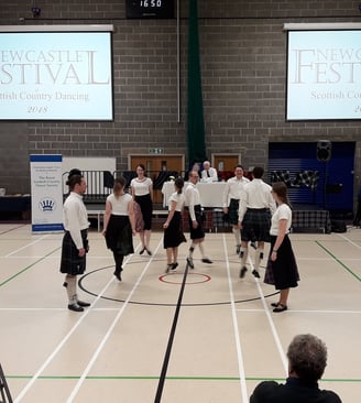 Team in kilts/black skirts and white shirts dancing a pas de basque.