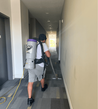 a man with a backpack vacuum cleaning the hallway carpet