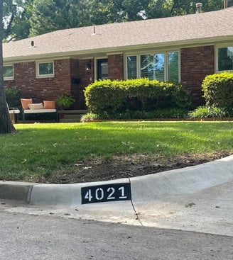 Brick house with a tan roof, shrubs, tree, and curb displaying house number '4021' in white on black