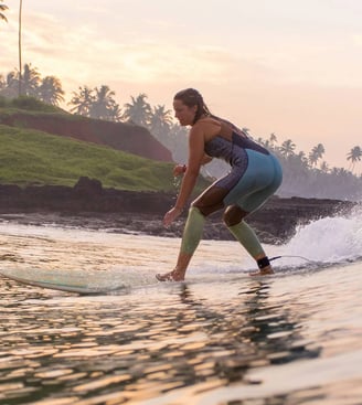 Girl surfing on a wave in Varkala, Kerala, with palm trees and cliffs in the background during sunrise.