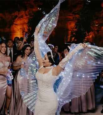 Novia muy contenta bailando con velo iluminado por luces led el día de boda, atrás de ella sus damas