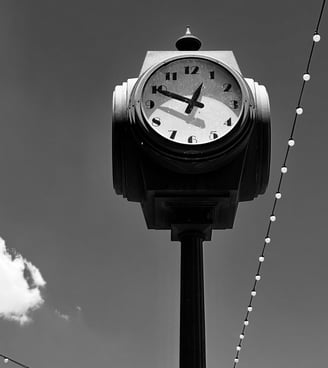 A black-and-white photograph of a vintage street clock mounted on a tall post against a clear sky.