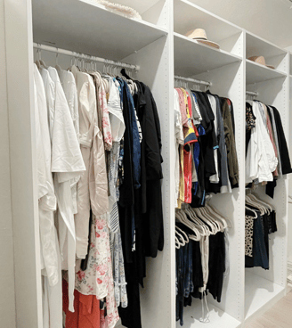 Open closet with color-coded clothing and neatly arranged hangers on white shelving.