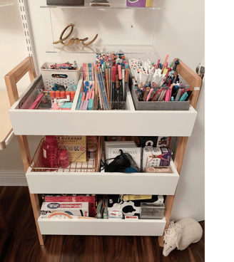 Organized art supply cart with labeled bins, pencils, markers, and craft materials.