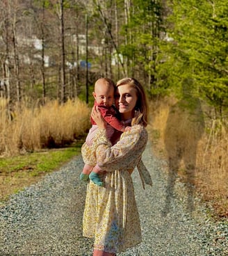 A mother holding baby on a gravel road at dusk, with the shadow of the father looming behind—tension of co-parenting & abuse 