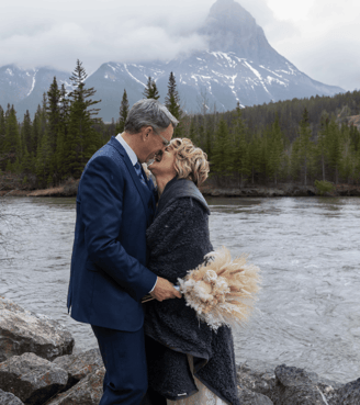 Bride and groom standing next to a river at the old train bridge in Canmore Alberta