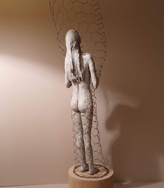 Clay sculpture of a female figure with hands gently placed on chest, surrounded by wire netting.