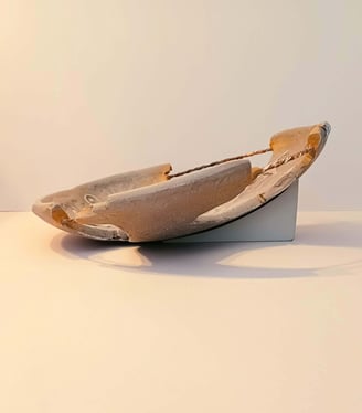 Side view of a bowl-like sculpture with embossed horse figures and symbols in rust/brown hues