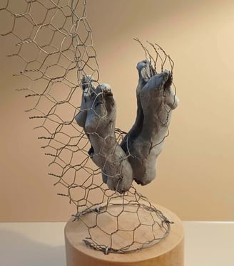 A sculpture of two female torsos, back to back, surrounded by wire netting, painted blue-greys