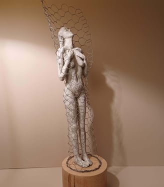 Clay sculpture of a female figure with hands gently placed on chest, surrounded by wire netting.