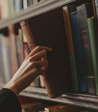 Hand reaching for a vintage book on a library shelf lined with books