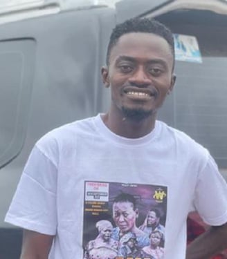 Lil Win in a white tee shirt standing infront of a car.