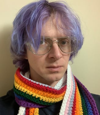 Tomkins with glasses on, wearing a rainbow scarf and with purple hair.