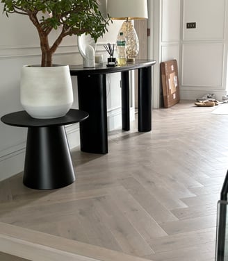 A light oak herringbone floor in a hallway with a step and small tables