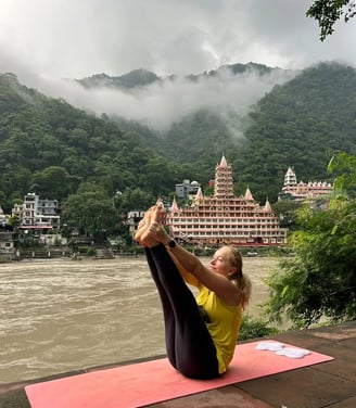 Eva practicing yoga by the Ganges River in Rishikesh with a temple in the background