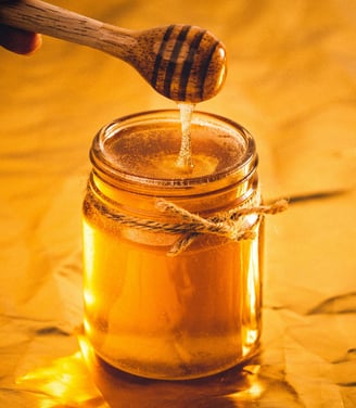 Jar of golden honey with a honey dipper dripping honey, set against a warm background.