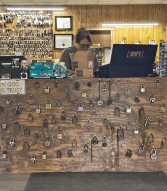 Emily, a female locksmith, assisting customers at the front counter of Jack's Locksmith in Burnsville, NC, wall of locks