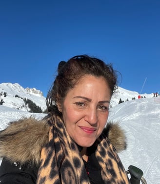 Praticienne en soins énergétiques souriante, photographiée devant un paysage de montagnes enneigées par une journée ensoleill