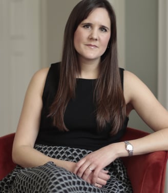 Photo of Anna Joyce CBT for insomnia therapist, sitting in red chair wearing a black geometric dress