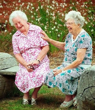 Two senior women laughing together, sitting outside