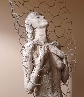 Clay sculpture of a female figure with hands gently placed on chest, surrounded by wire netting.