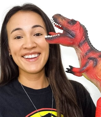 A half Chinese woman holding a dinosaur toy wearing a Jurassic Park t-shirt