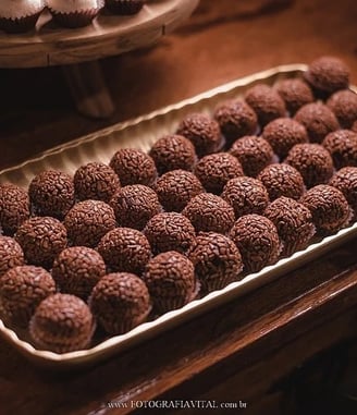 Uma bandeja cheia de brigadeiros de chocolate cuidadosamente dispostos sobre uma mesa de madeira, ce