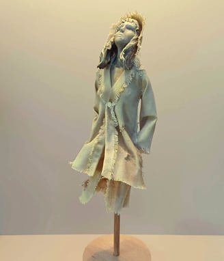 Clay and canvas sculpture of a female figure gazing upwards, wearing windswept, ragged clothes.