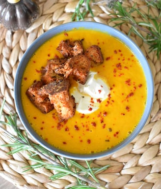 a bowl of pumpkin soup with croutons and cream 