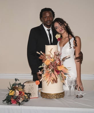 Bride & Groom posing for a photo by their three tiered cake before cutting