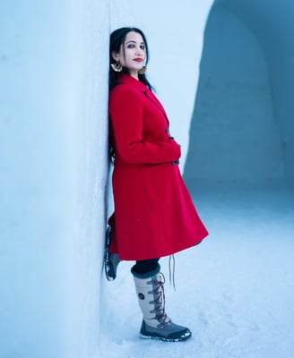 a woman in a red coat and boots standing in the snow and leaning on snow wall