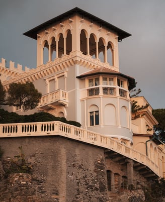 Elegant, cream-colored historical villa with ornate arches perched on a rocky cliff in Bogliasco