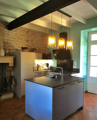 Cuisine beige, plan de travail en ardoise, cuve inox et robinetterie inox brossée. Hotte murale noir