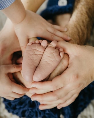 Mains de toutes la famille qui tiennent les pieds du nouveau-né