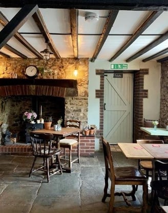 a table and chairs near to a wood burning fire with a clock above it