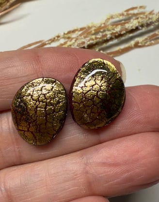 a person holding two gold earrings with gold foil