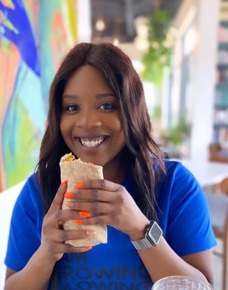 a plus size black woman nutritionist in a blue shirt is holding a sandwich